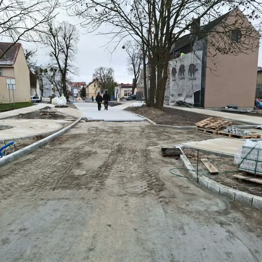 Ulica podczas przebudowy z nowymi chodnikami i dwiema osobami idącymi w oddali.