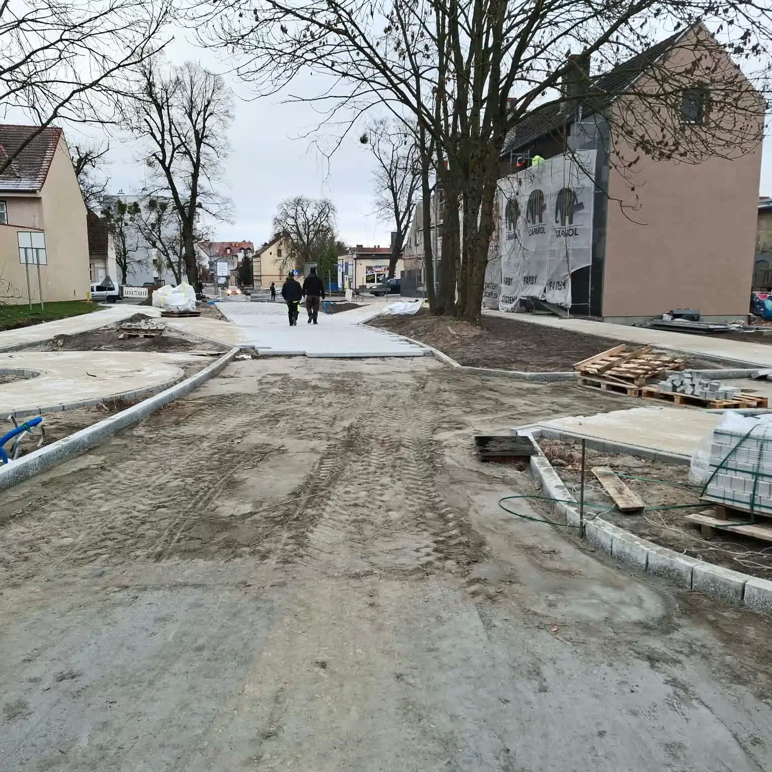 Ulica podczas przebudowy z nowymi chodnikami i dwiema osobami idącymi w oddali.