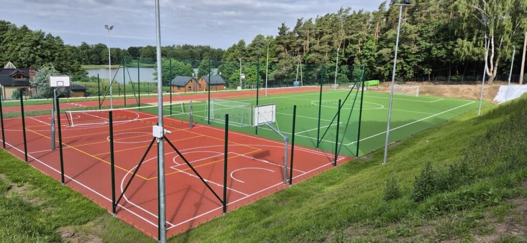 Nowoczesny kompleks sportowy położony przy jeziorze i lesie. Na terenie znajdują się zielone boisko piłkarskie, czerwone boiska wielofunkcyjne, bieżnia, bramki, kosze i oświetlenie.